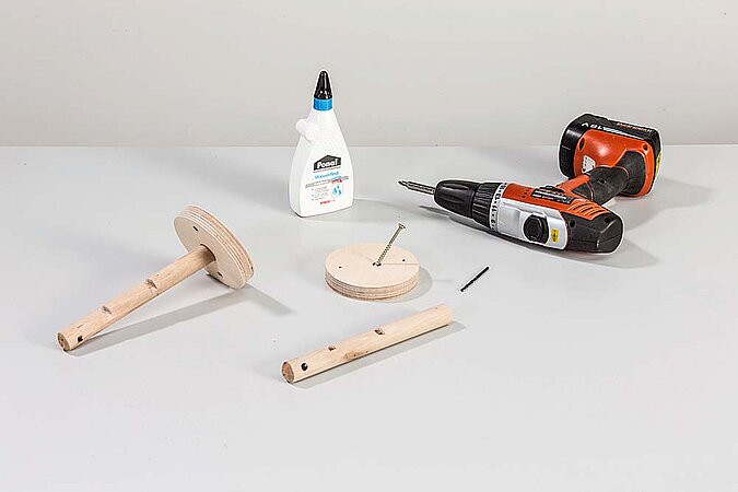 Einzelteile für Haken aus Pömpeln liegen mit Holzleim, Schraube und Akkuschrauber auf einer Werkbank