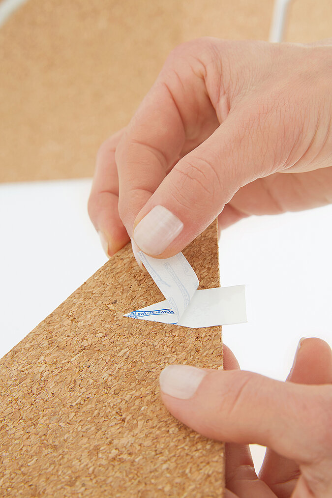 Um eine Pinnwand aus Kork im Fuchsdesign aufzuhängen, werden Powerstrips aufgeklebt