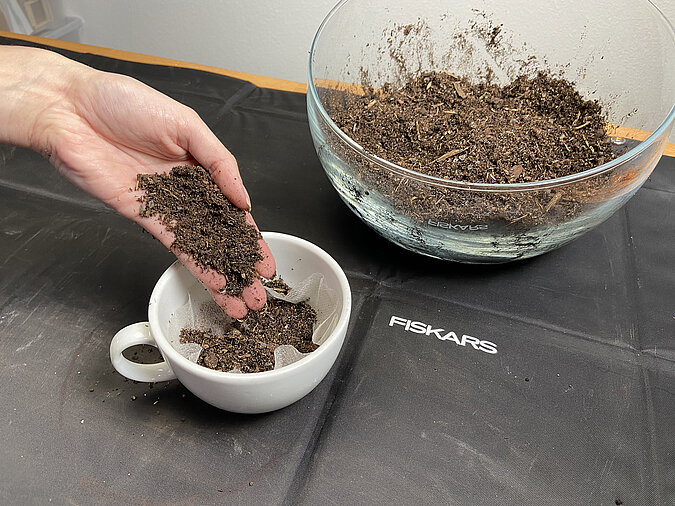 Tassengarten basteln und Blumenerde von Hand in die Tasse einfüllen