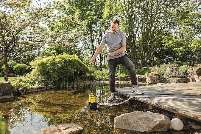 Mann reinigt Gartenteich mit einer Teichpumpe