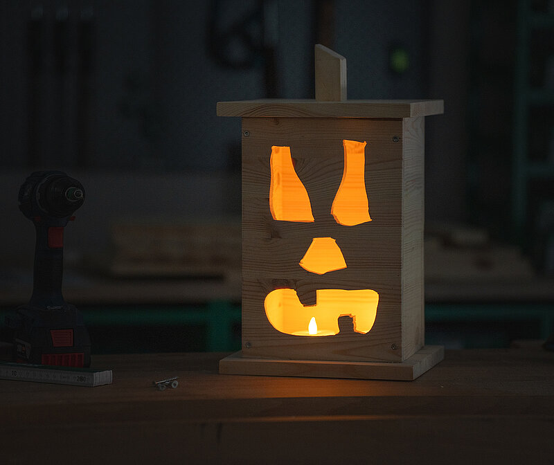 Halloween-Laternen selber bauen: selbstgemachte Laterne aus Holz mit ausgeschnittenem Gesichtsmotiv, leuchtend im Dunkeln vor einer Haustür für stimmungsvolle Halloween-Deko