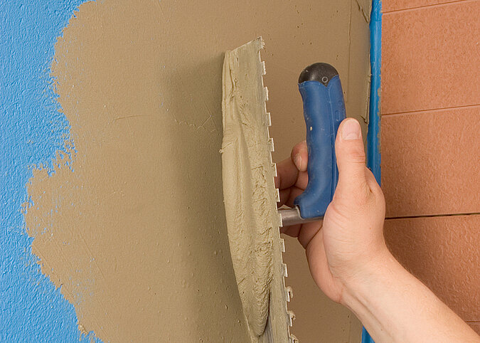 Fliesen an die Wand kleben Auftragen von Fliesenkleber mit Glättkelle auf die vorbereitete Wandfläche