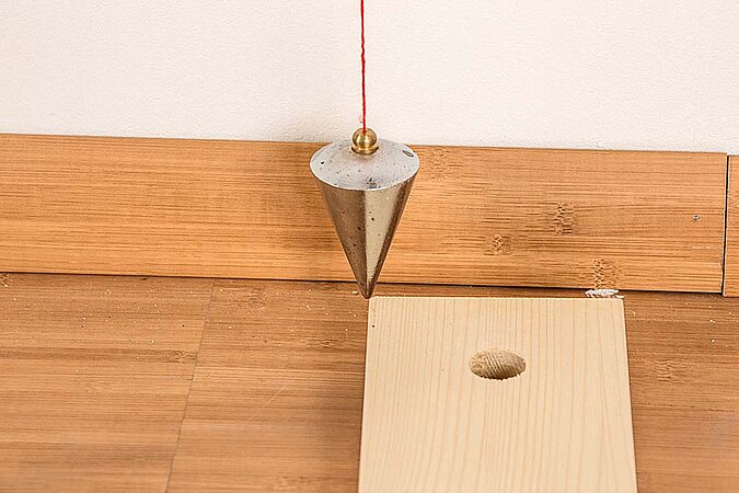 Lot hängt über dem unteren Holzbrett und markiert die Position für den Raumteiler aus Birkenstämmen am Boden