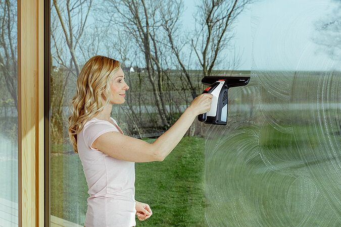 Frau im T-Shirt putzt Fenster mit einem Fenstersauger