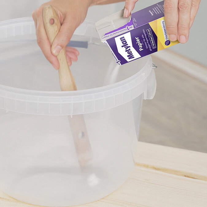 Wände richtig tapezieren: Tapetenkleister wird aus einer Metylan-Packung in einen Eimer mit Wasser eingerührt – Vorbereitungsschritt für sauberes und dauerhaftes Tapezieren