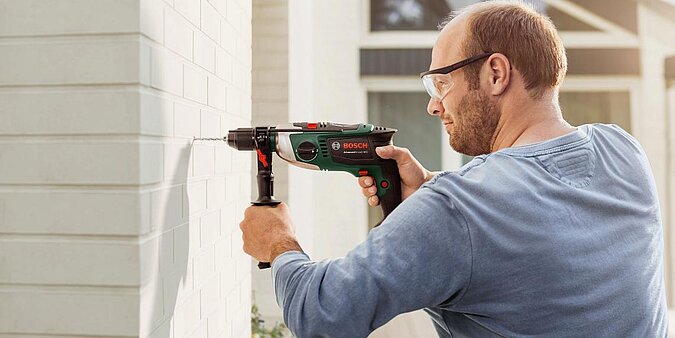 Mann mit Schutzbrille bohrt ein Loch in eine Hauswand