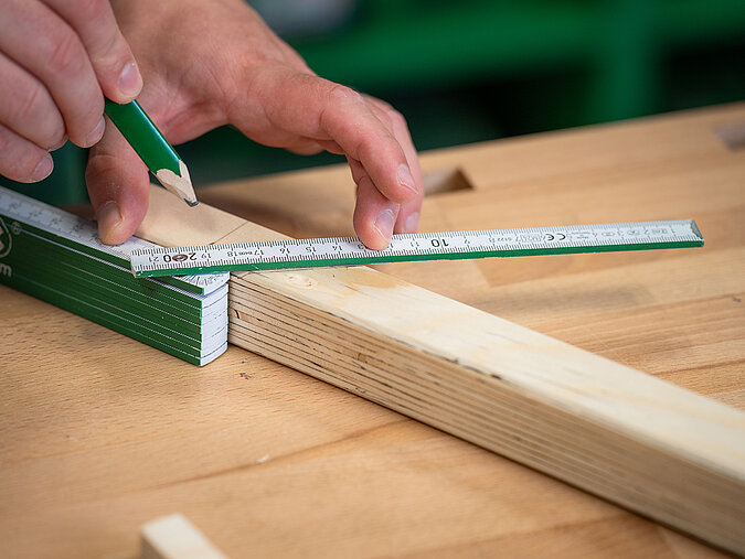 Halloween-Laternen selber bauen: Holzleiste wird mit Bleistift markiert, um sie für den Zuschnitt der Laterne vorzubereiten
