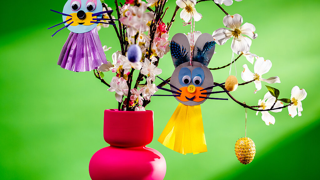 Nahaufnahme eines Osterstrauches mit selbstgebastelten Hasenanhängern aus Tonpapier vor grünem Hintergrund