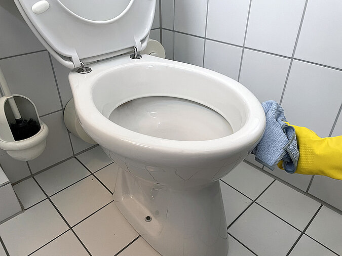 Frühjahrsputz: Hand mit gelben Gummihandschuh putzt Toilette