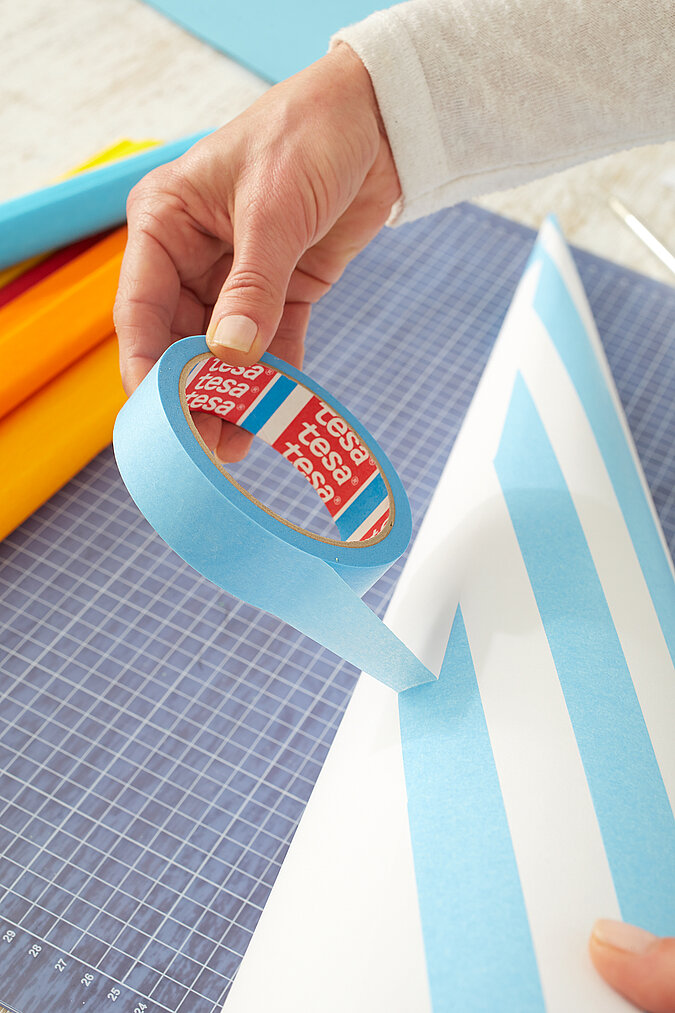 Auf einen weißen Schultüten-Rohling werden blaue Malerkrepp-Streifen für den Raketen-Look geklebt