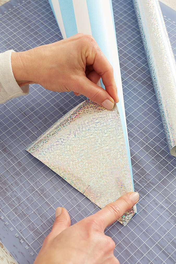 Eine Schultütenspitze wird mit silberner Halogrammfolie beklebt