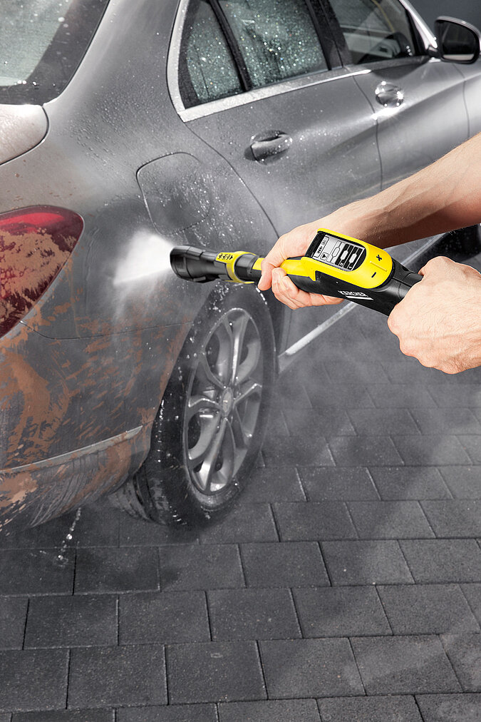 Auto selbst waschen mit Hochdruckreiniger – Nahaufnahme einer Hand, die den Wasserstrahl auf das Autorrad richtet, um Schmutz und Bremsstaub gründlich zu entfernen.
