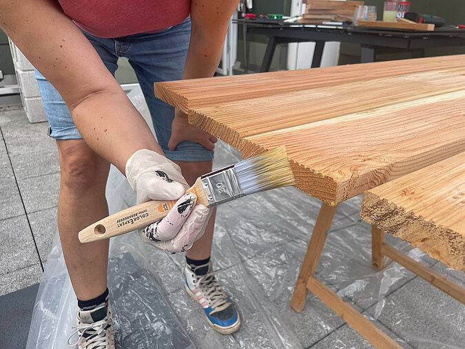 Grillplatz für die Terrasse bauen: Kanten der Holzdielen werden sorgfältig mit Holzöl behandelt – wichtiger Schritt für optimalen Witterungsschutz und lange Haltbarkeit der DIY-Grillstation.