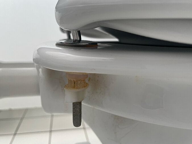 Klodeckel wechseln & pflegen – Unterseite der Toilettenbefestigung mit Schraube und Kunststoffhalterung