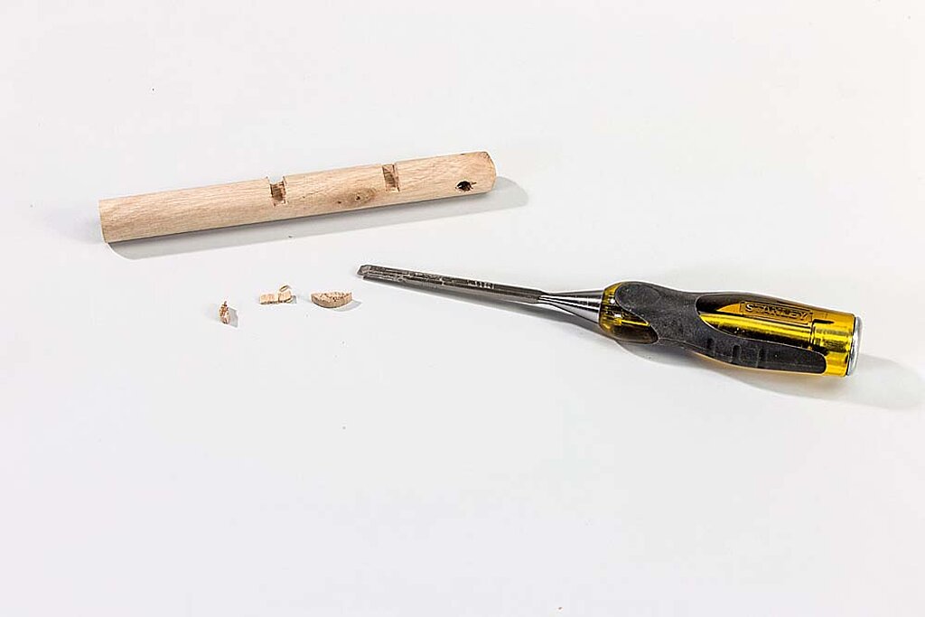 Kerben werden mit einem Stechbeitel in den Pömpelstiel für einen Haken am Raumteiler aus Birkenstämmen gearbeitet