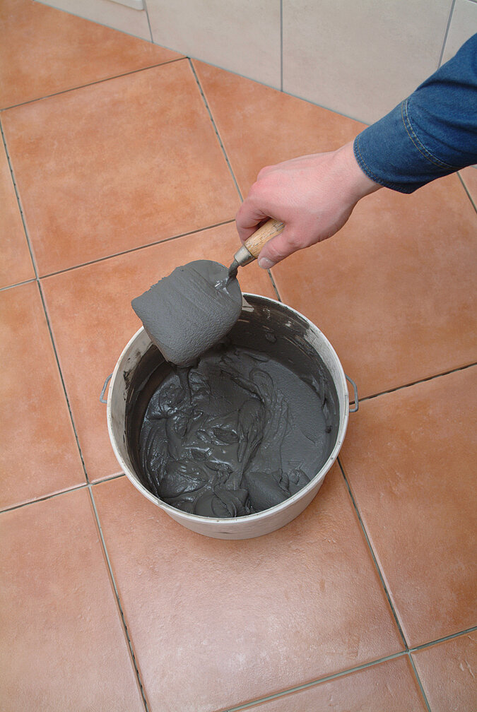 Hand taucht eine Kelle in Eimer mit Fugenmoertel