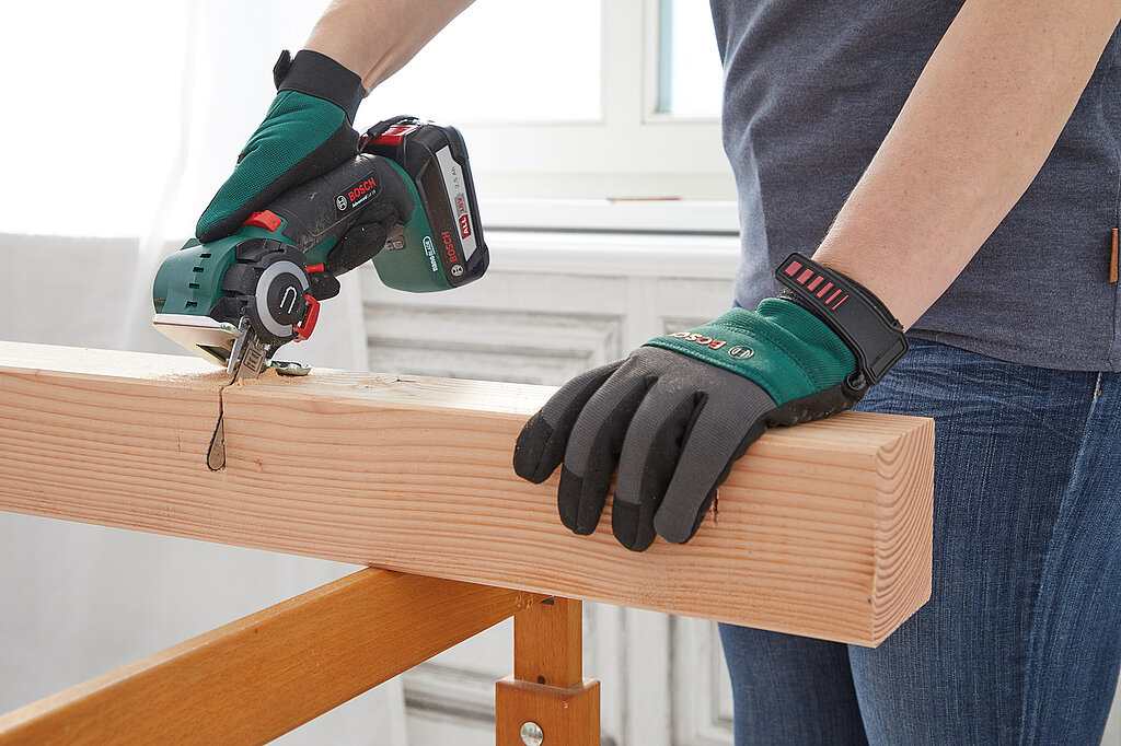 Hände mit Arbeitshandschuhe sägen mit einer Akku-Säge ein Stück Kantholz ab