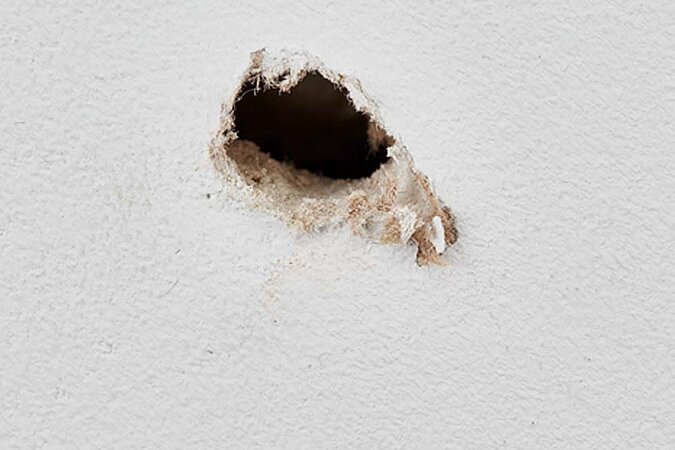 Ausgefranztes und großes Bohrloch auf einer weißen Wand 