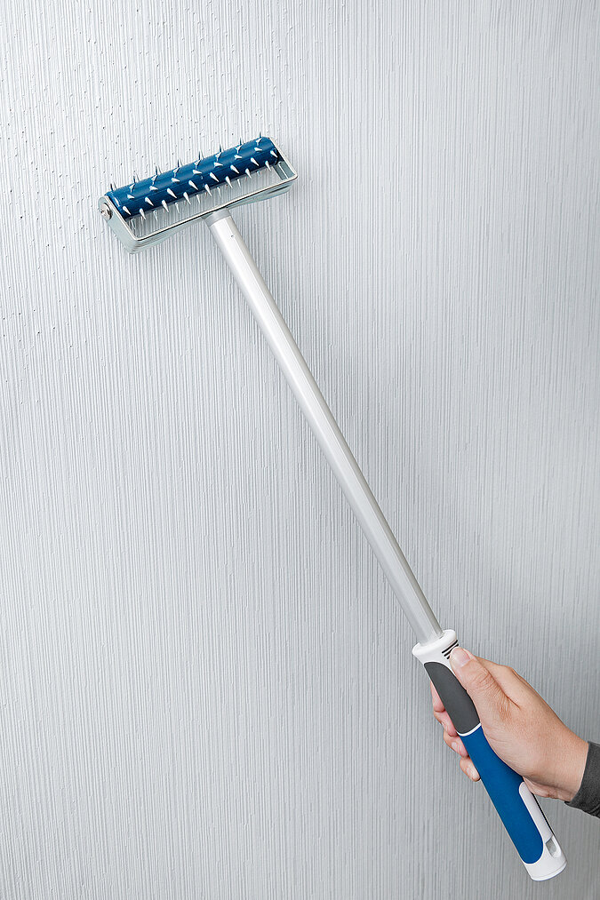 Wände richtig tapezieren – praktische Tipps zum Tapetenentfernen: Hand führt eine Igelwalze über die alte Tapete, um diese perforiert für das anschließende Einweichen vorzubereiten.