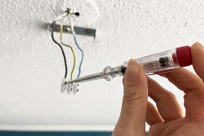 Die aus der Decke kommenden Stromkabel werden mit einem Spannungsprüfer auf Stromfluss überprüft. Der Stromprüfer zeigt keinen Stromfluss an.