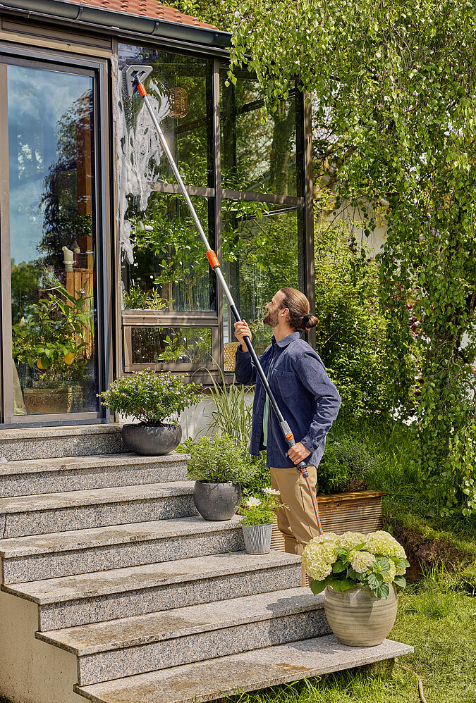 Mann wäscht Panoramafenster von Wintergarten mit Stielbuerste