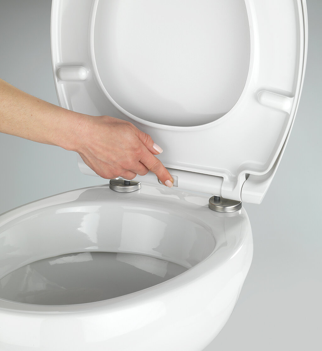 Klodeckel wechseln & pflegen – Hand zeigt Entriegelungstaste am WC-Sitz zur einfachen Demontage