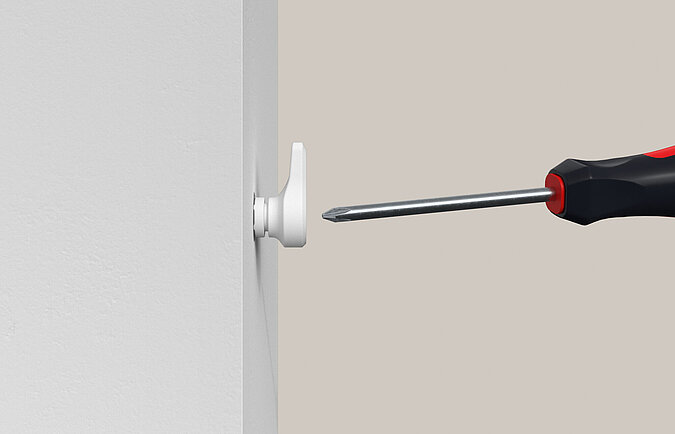Ein Kunstoffhaken "EasyHook" wird mit einem Schraubendreher in die Wand geschraubt