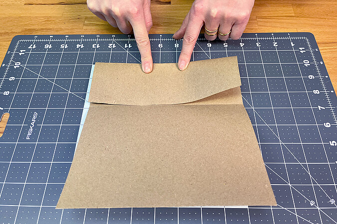 Ein Blatt Bastelpapier wird auf einer Bastelunterlage mittig gefaltet
