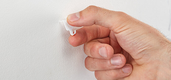 Hand drückt eine Bilderkralle in die Wand