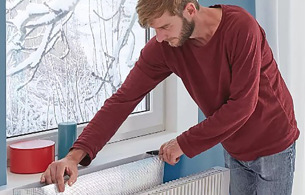 Mann bringt Isolierfolie hinter Heizung an