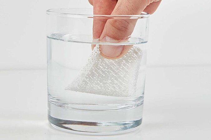 Reparaturvlies wird in einem Glas mit Wasser befeuchtet, um ein großes Bohrloch zu retten 