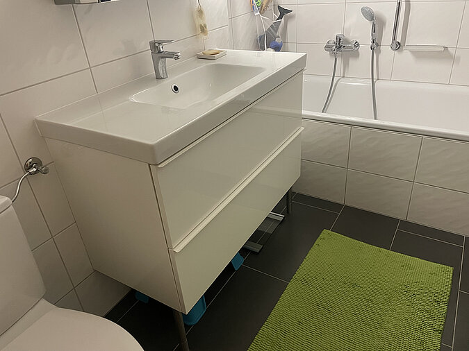 Badezimmer mit großen weissen Kacheln, Waschbecken mit Unterschrank und Badewanne
