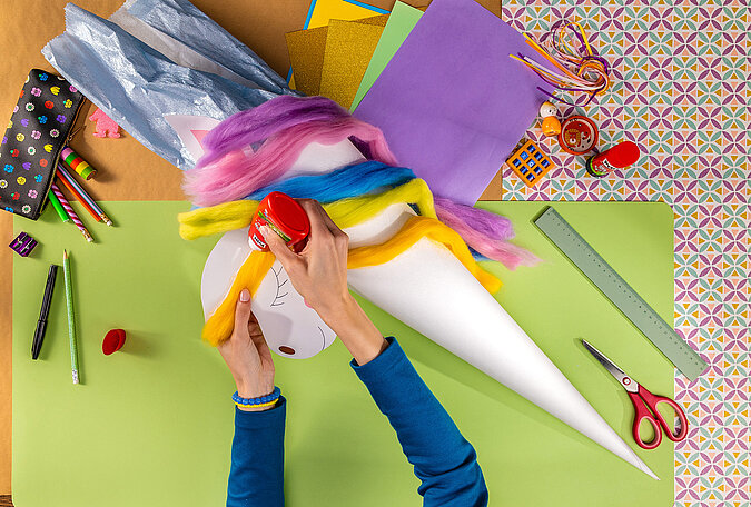 Schultüte Einhorn basteln beim Aufkleben der bunten Regenbogenmähne auf die Schultüte