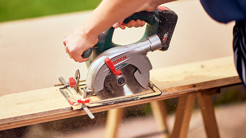 Eckbank Küche bauen – Holzbrett wird mit einer Handkreissäge präzise zugeschnitten, um Bauteile für eine Küchen-Eckbank vorzubereiten
