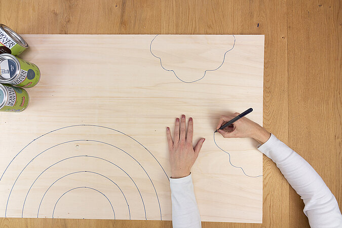 Wandleuchte im Regenbogen-Design bauen – Hand zeichnet detaillierte Bögen auf Holz, um die Regenbogenform für die spätere Leuchte vorzubereiten.