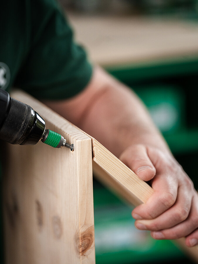 Für eine Helmgarderobe verschraubt ein Mann 3 Bretter zu einem Dreieck zusammen