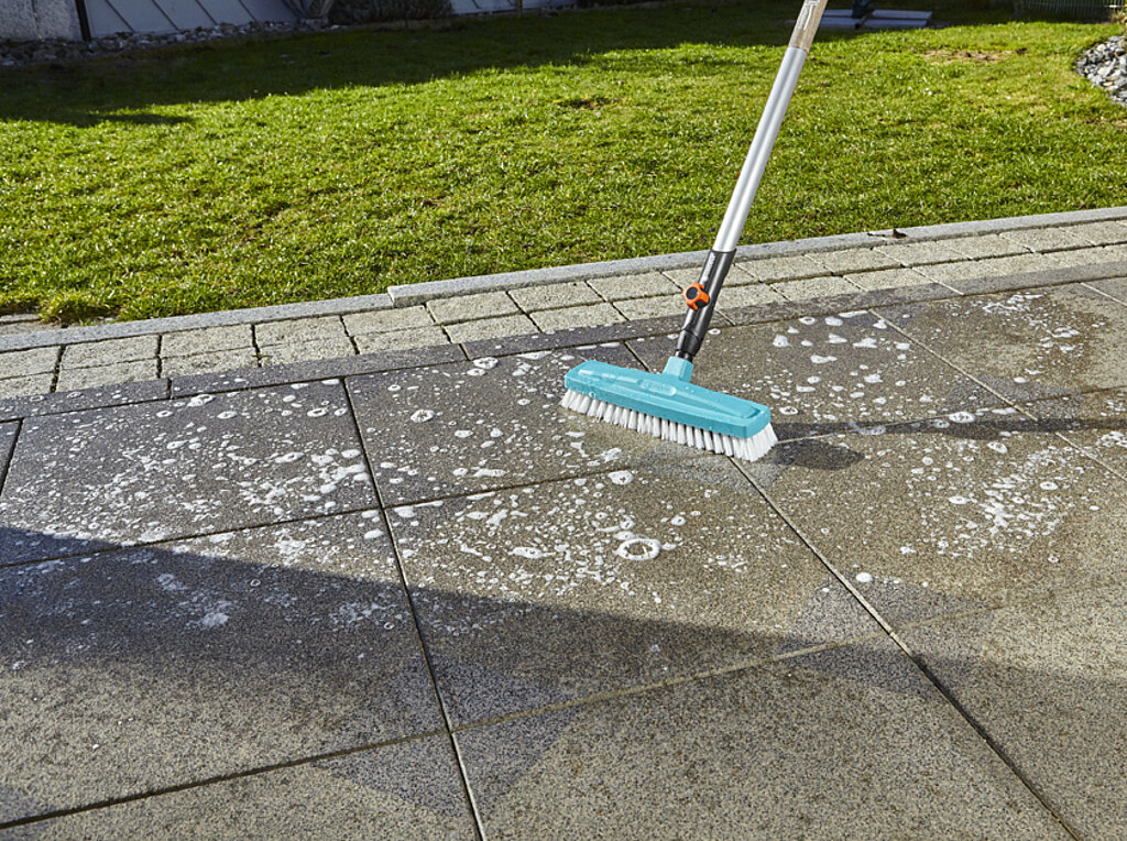 Schrubber wischt auf Terrasse durch Putzwasser