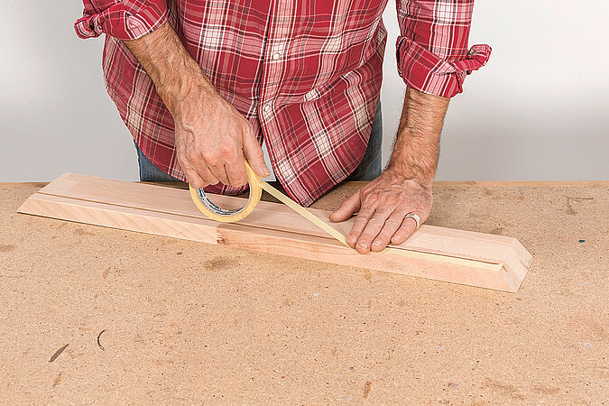 Wandgarderobe aus Kickerfiguren bauen mit Kreppband zum Markieren der Positionen für die Kickerstangen am Holzrahmen
