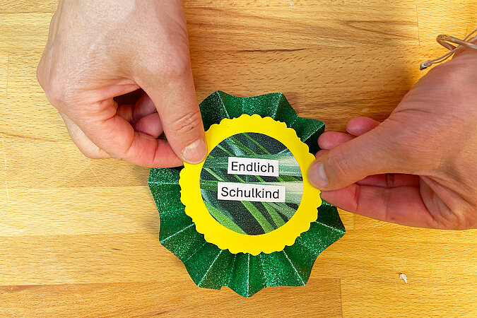Einschulung Orden basteln mit aufgeklebtem Schriftzug „Endlich Schulkind“ auf der grünen Papierrosette