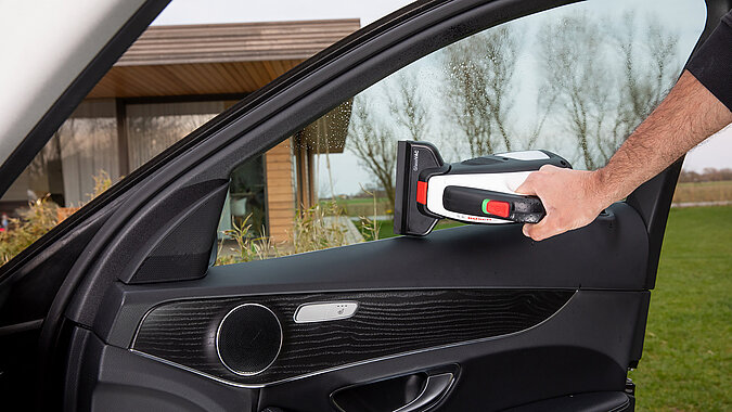 Auto selbst waschen Fensterreinigung – Hand wischt mit elektrischem Fenstersauger die Autoscheibe innen für streifenfreien Glanz.