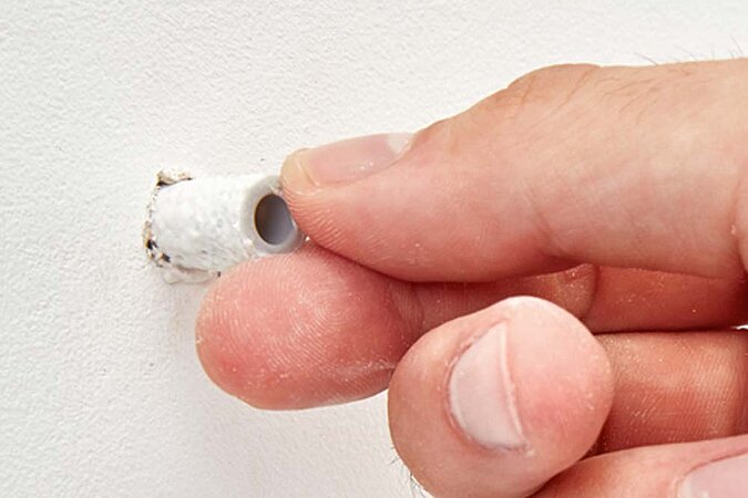 Eine Hand steckt den mit Reparaturvlies umwickelten Dübel in das Bohrloch