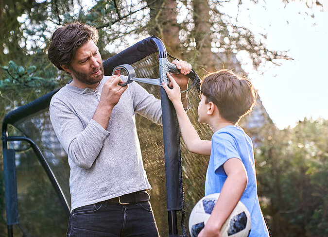 Vater und Sohn reparieren den Pfosten eines Fussballtores mit Klebeband 