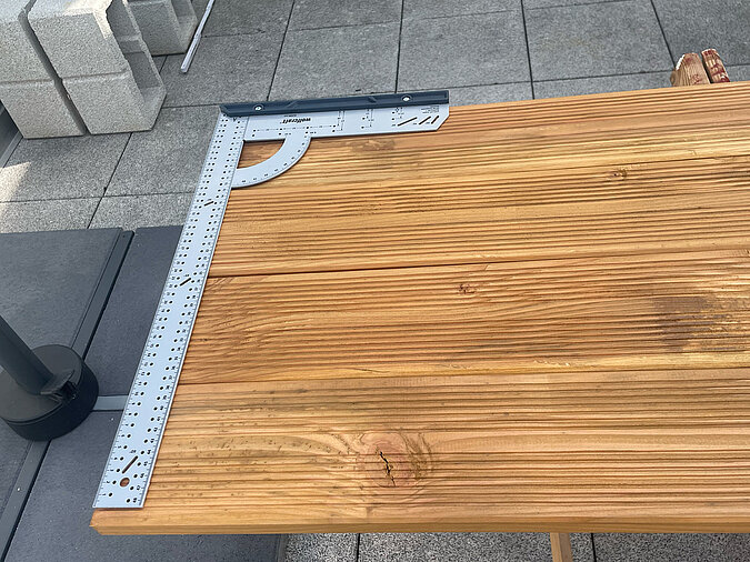 Grillplatz für die Terrasse bauen: Metallwinkel zur exakten Ausrichtung der Ablagebretter aufgelegt – wichtiges Hilfsmittel für präzise Winkel und saubere Verarbeitung beim DIY-Projekt.