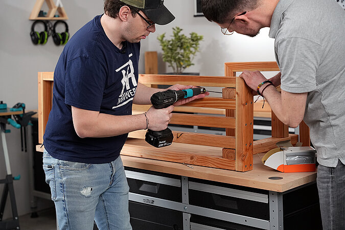 Zwei Männer befestigen den Fuss für eine Gartenbank am Grundrahmen