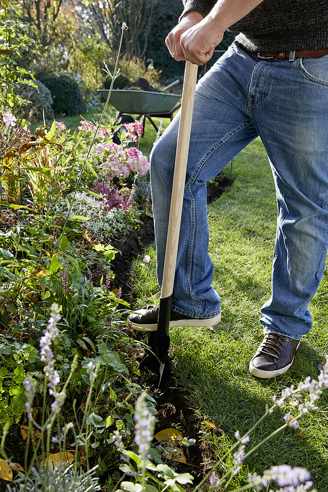 Mann sticht mit einer Gartenschaufel eine Beetumrandung aus