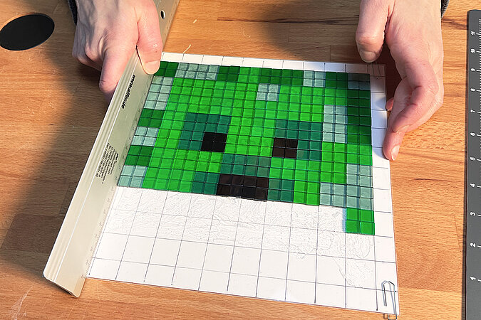 Creeper-Deko-Leuchte basteln beim Ausrichten der farbigen Mosaiksteine auf der Rastervorlage zur Gestaltung des Creeper-Gesichts