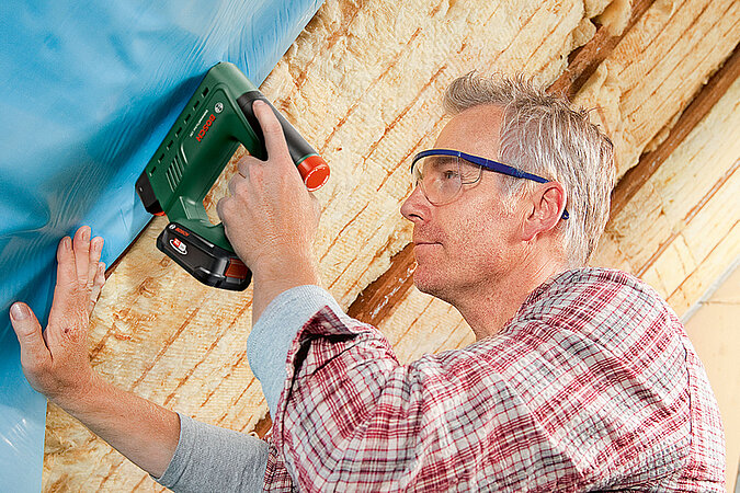 Handwerker bringt Dachdämmung an, um das Dach fachgerecht energetisch zu sanieren und den Wärmeverlust nachhaltig zu reduzieren.