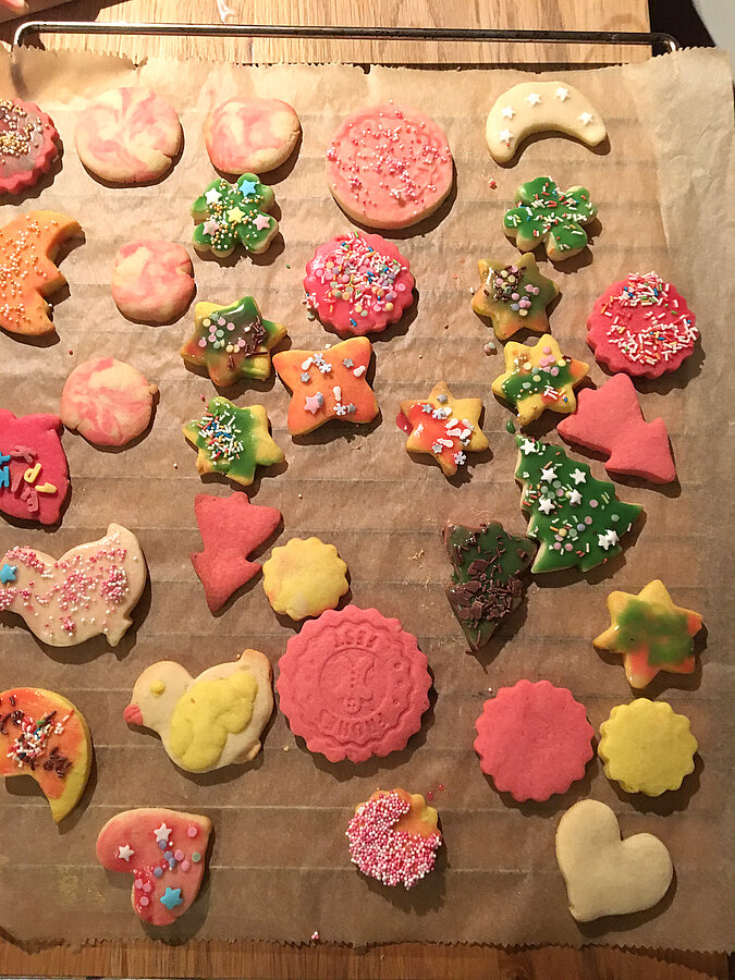 Lernturm für Kinder bauen und gemeinsam fantasievoll ausgestochene Weihnachtskekse dekorieren, bunte Plätzchen auf Backblechen und Arbeitsfläche verteilt
