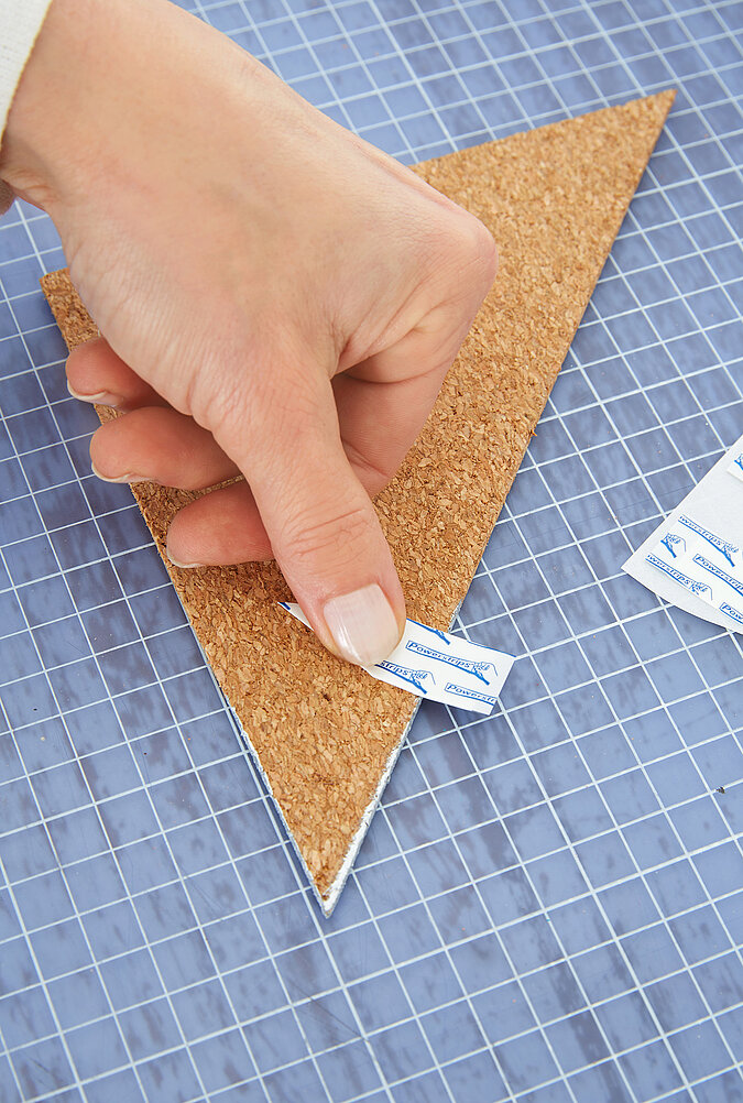 Um eine Pinnwand aus Kork im Fuchsdesign aufzuhängen, werden Powerstrips aufgeklebt