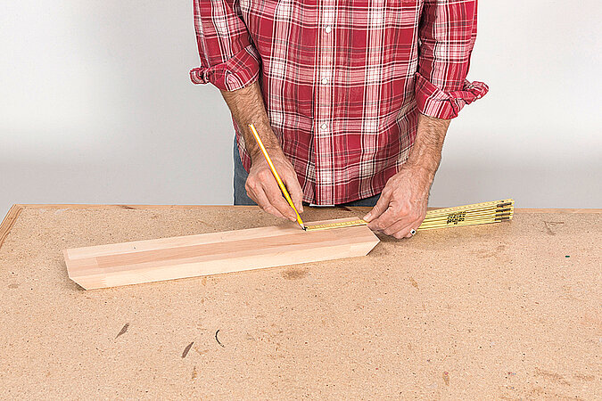 Wandgarderobe aus Kickerfiguren bauen mit Maßband und Bleistift beim Anzeichnen der Bohrpunkte auf dem Holzrahmen